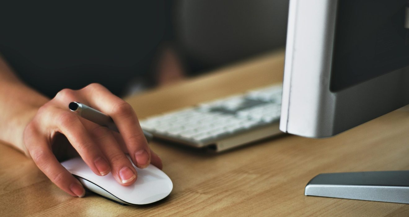Free A hand using a wireless mouse at a modern desk setup with a computer and keyboard. Stock Photo